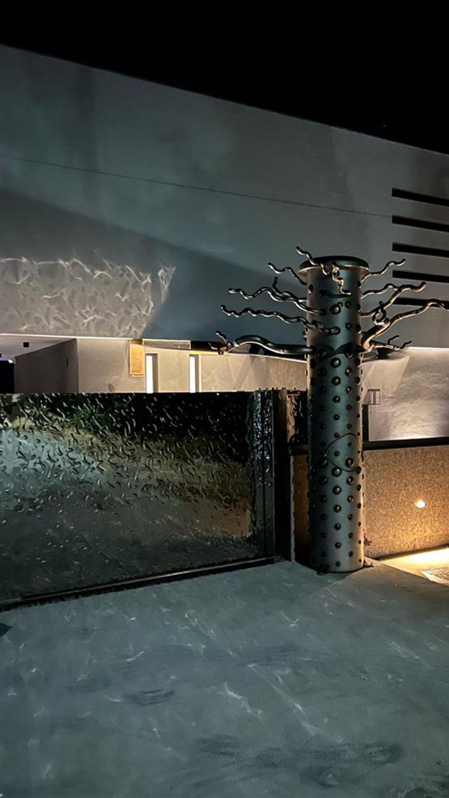 Portail d’entrée avec surface en acier inoxydable structurée en vagues et accès éclairé de nuit