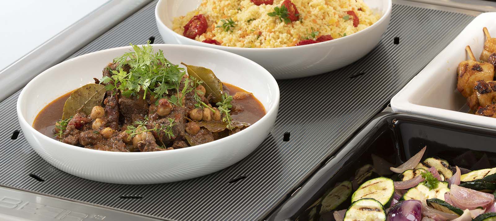 Bols avec plats chauds sur plaque chauffante nervurée en acier inoxydable en vitrine