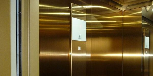 Vue intérieure d’une cabine d’ascenseur avec parois en acier inoxydable Oro HL doré et panneau d’affichage intégré