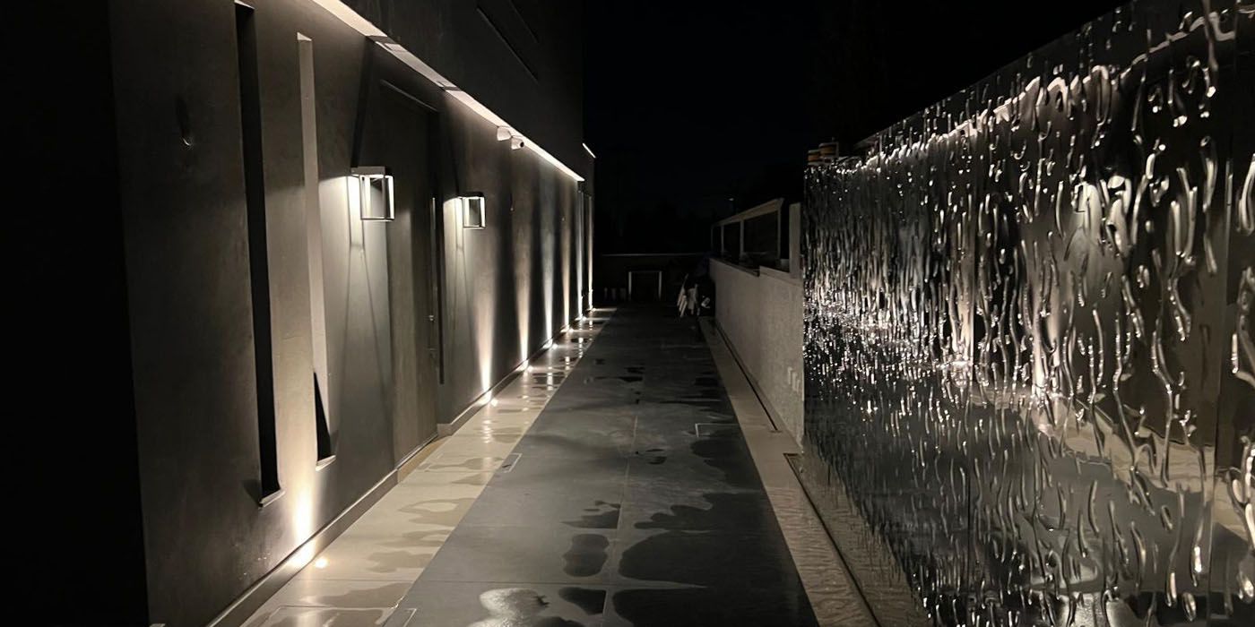 Allée éclairée le long d’un mur avec surface en acier inoxydable réfléchissante à structure ondulée de nuit