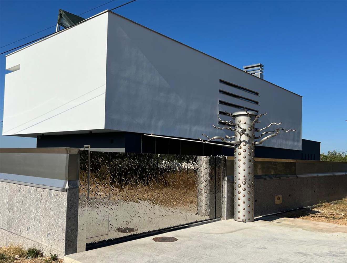 Portail d’entrée moderne avec surface en acier inoxydable réfléchissante à structure ondulée devant un bâtiment blanc de jour