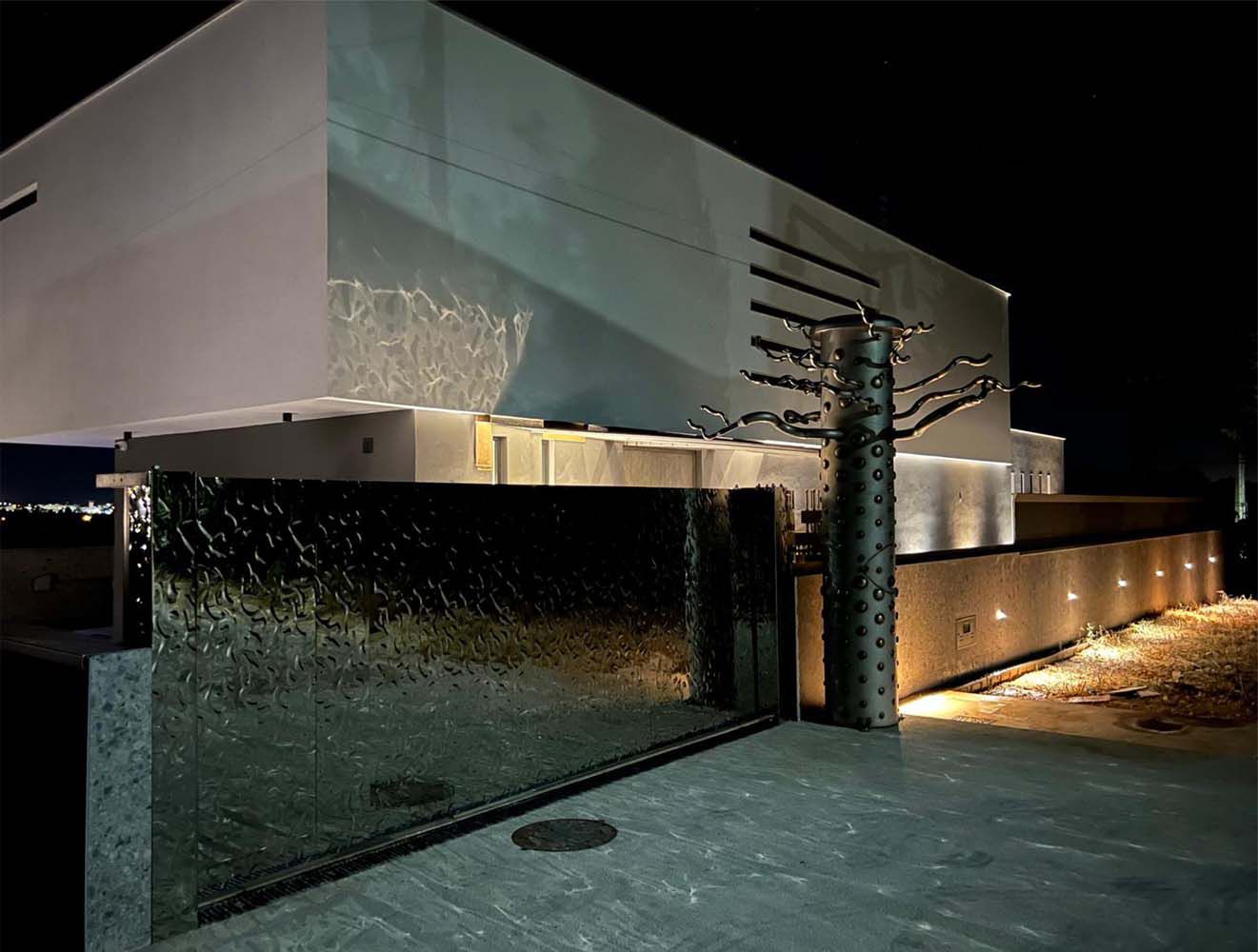 Portail d’entrée moderne avec surface en acier inoxydable réfléchissante à structure ondulée devant un bâtiment résidentiel éclairé de nuit