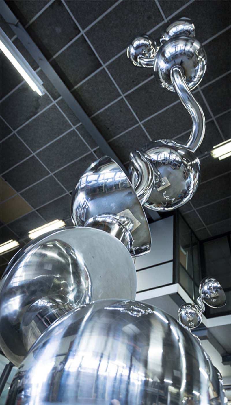 Polished stainless steel spheres and curved tube segment in a workshop hall with ceiling lighting