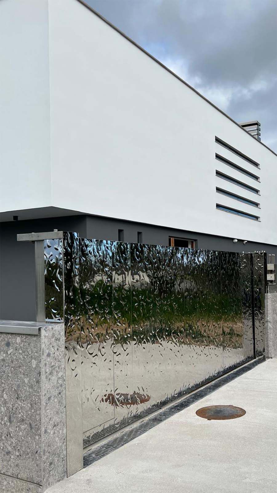 Portail d’entrée moderne avec surface en acier inoxydable réfléchissante à structure ondulée sur bâtiment blanc