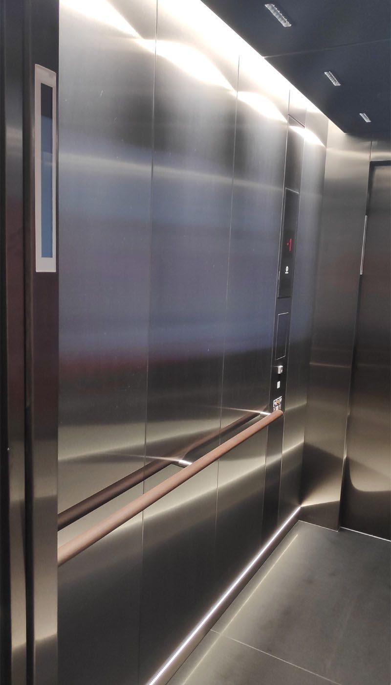Vue latérale de l’ascenseur multimédia avec parois en acier inoxydable satiné et main courante