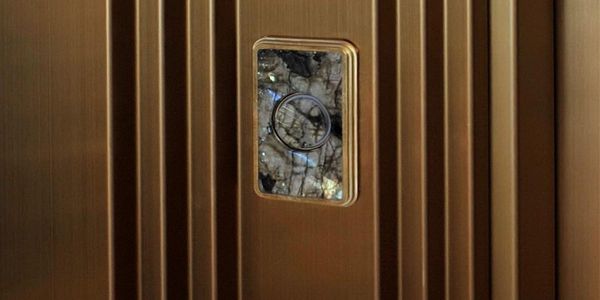 Détail d’une porte d’ascenseur dorée en acier inoxydable avec hublot et structure verticale