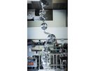 Tall sculpture made of polished stainless steel spheres and curved tube elements in a workshop hall