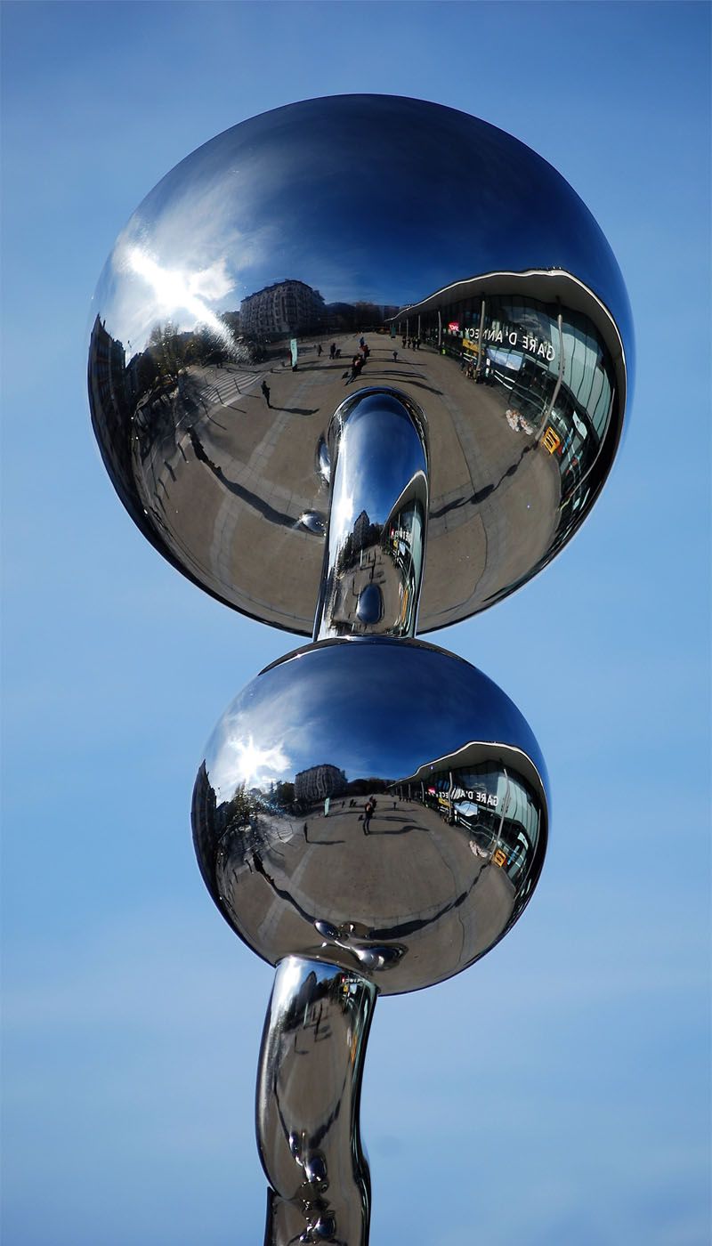 Two polished stainless steel spheres arranged vertically with connecting element against a blue sky