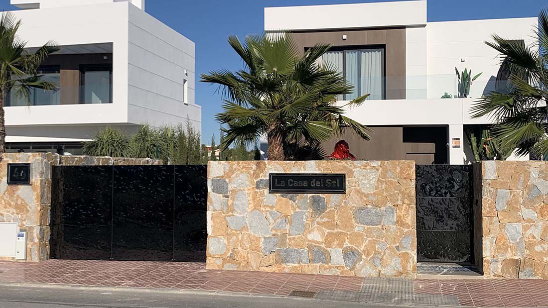 Portail moderne en acier inoxydable noir entre murs en pierre naturelle avec villa en arrière-plan