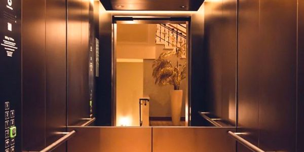 Cabine d’ascenseur avec revêtements muraux en acier inoxydable couleur bronze et porte ouverte vers le couloir